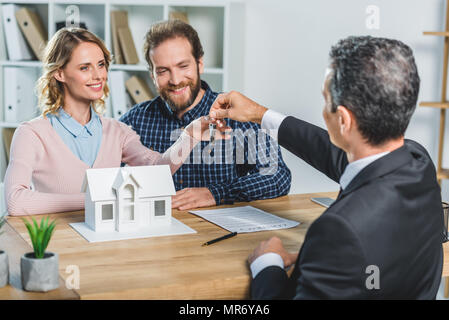 Portrait of happy couple obtenir les clés à nouveau accueil de realtor in office Banque D'Images