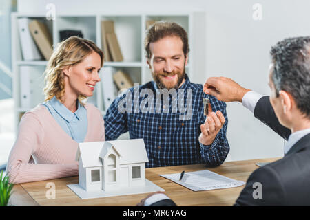 Portrait of happy couple obtenir les clés à nouveau accueil de realtor in office Banque D'Images