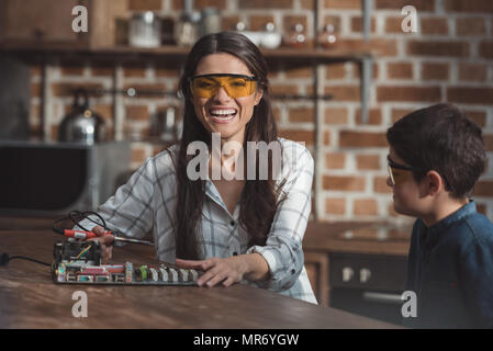 Smiling woman wearing lunettes de protection et de travail sur l'électronique projet scolaire avec son petit fils Banque D'Images