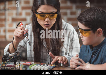 Petit-fils et sa belle mère travaillant avec fer à souder sur projet de l'école de l'électronique Banque D'Images