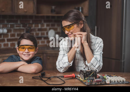 Petit-fils et sa jeune mère dans des lunettes assis à table avec elle sur la carte mère Banque D'Images