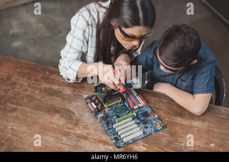 Petit-fils et de sa mère en travaillant avec des lunettes de protection fer à souder sur carte mère. Banque D'Images