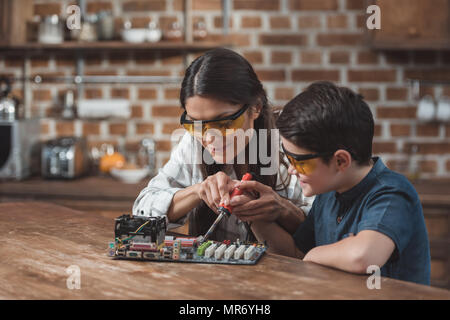 Petit-fils et sa belle mère travaillant avec fer à souder sur carte mère. Banque D'Images