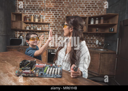 Petit-fils et sa belle-mère high fiving tout en travaillant sur la carte mère d'un ordinateur à la maison Banque D'Images