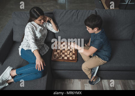 Un petit garçon se déplacer dans les échecs tout en jouant avec sa maman sur la table dans la salle de séjour Banque D'Images