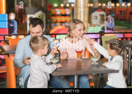 Famille avec deux enfants de manger savoureux desserts et père en utilisant smartphone dans cafe Banque D'Images