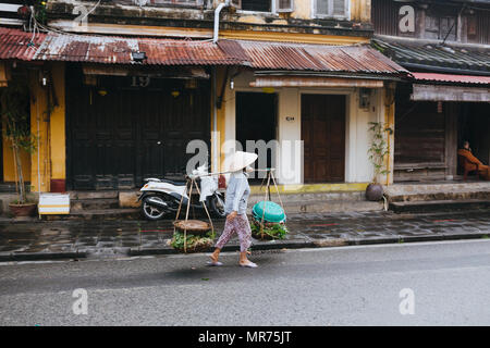 HOI AN, VIETNAM - 03 janvier, 2018 : vietnamienne portant des paniers de plantes vertes et de marcher sur la rue à Hoi An, Vietnam Banque D'Images