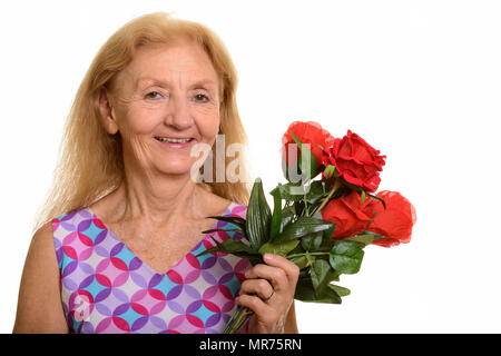 Studio shot of senior woman smiling and holding red roses Banque D'Images