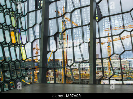 Harpa, une salle de concert et centre de conférence à Reykjavik, Islande. Le bâtiment dispose d'une façade en verre de couleur distinctif inspiré par le paysage de basalte de l'Islande. La structure se compose d'un cadre en acier revêtus de panneaux de verre en forme géométrique & tubes hexagonal de couleurs différentes donnant une vue sur le site de construction voisin des grues, et le développement. Banque D'Images