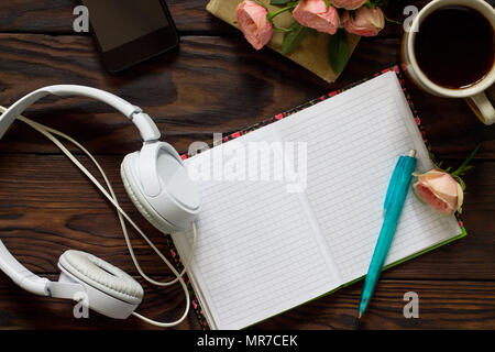 Smartphone, le casque et l'ordinateur portable ouvert avec des pages blanches à côté de tasse de café sur la table en bois. Vue supérieure de la télévision mise de fond. Banque D'Images