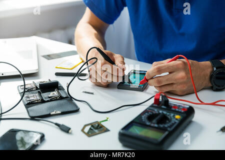Technicien en réparation smartphone - contrôler le téléphone avec le multimètre Banque D'Images