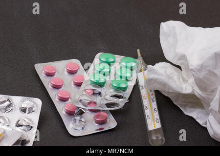 Pilules, thermomètre, serviette de papier froissé et serviette sur elle. Vue de dessus, medicine concept photo. Fond noir Banque D'Images