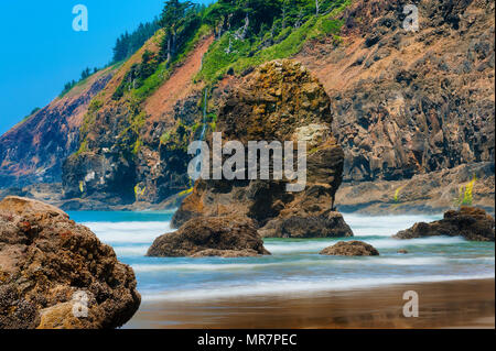 Scène de plage paysage où de grandes roches intertidales briser le surf entrant. Banque D'Images