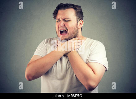 Chunky homme froncer et étouffantes ayant des allergies et tenir la main sur le cou avec les yeux fermés. Banque D'Images