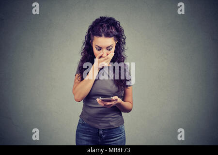 Jeune fille étonné et bouche couvrant la lecture des nouvelles sur smartphone ayant une forte réaction sur fond gris. Banque D'Images