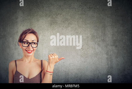 Laughing woman à la recherche sur le côté et à l'opposé avec pouce sur wall background Banque D'Images