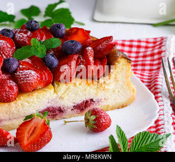 Cheesecake fait de fromage blanc et de fraises fraîches sur une plaque en céramique blanc, décorée avec des fraises et des bleuets Banque D'Images