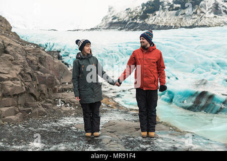 Beau young couple holding hands and smiling mutuellement tout en se tenant près de l'Islande, Glacier Svinafellsjokull Banque D'Images