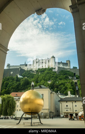 Place Kapitelplatz, Salzbourg, Autriche. Sculpture sphaera (Man sur Mozart Golden Ball) avant-plan et forteresse de Hohensalzburg médiévale derrière. Banque D'Images