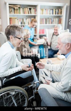 Senior woman in wheelchair talking à homme fiend en maison de soins. Banque D'Images