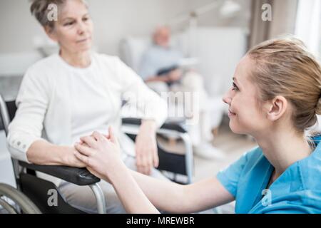 Travailleur de soins rassurant senior woman in wheelchair en maison de soins. Banque D'Images