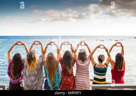 Sept belles jeunes filles à partir de l'arrière fait un coeur avec les mains à l'océan au coucher du soleil dans l'attente de l'activité de loisirs de vacances. friendshipt Banque D'Images