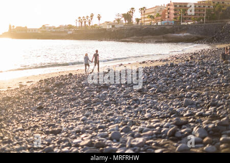 Romantic couple marche sur le rivage de la plage près de vagues et marées de l'océan. rocks beach pour la famille et les gens en amour avec coucher du soleil doré sur le backg Banque D'Images