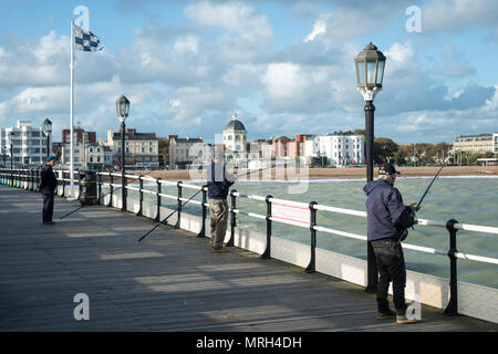 Les hommes de la pêche sur la jetée de Worthing dans un ciel ensoleillé mais venteux nuageux jour à Worthing dans le West Sussex, Angleterre, Royaume-Uni. Banque D'Images