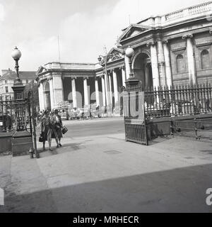 Années 1940, historique, deux dames marchent à travers l'entrée fermée ouverte de Trinity College, un campus universitaire historique à College Green, dans le centre-ville de Dublin, Irlande, Banque D'Images