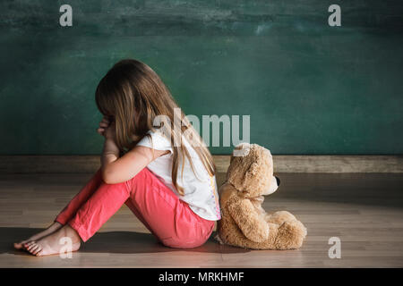 Petite fille aux ours assis sur le plancher de salle vide. Concept de l'autisme Banque D'Images