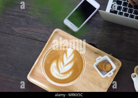 Tasse de café avec de belles latte art et ordinateur portable dans les mains de la jeune fille sur la table en bois Banque D'Images