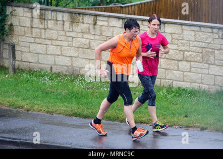 Chippenham, UK, 27 mai 2018. Deux femmes sur la course sont illustrés bravant la forte pluie à Chippenham aussi lourds orages font leur chemin à travers le sud de l'Angleterre. Credit : lynchpics/Alamy Live News Banque D'Images