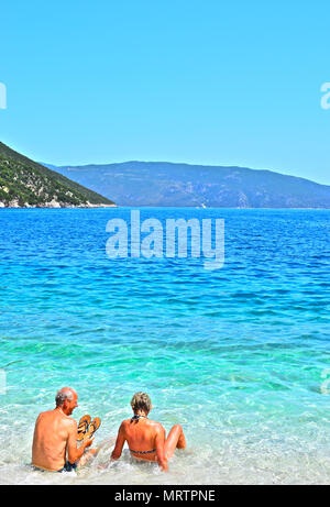 Un vieux couple s'amusant et profiter assis dans les eaux cristallines de la mer Ionienne, à proximité de Plage d'Antisamos Sami, Kefalonia, Grèce. Banque D'Images