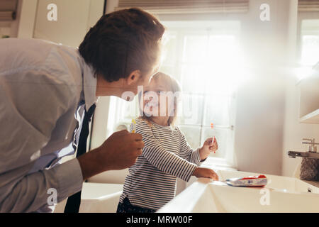 Père et fille se brosser les dents dans la salle de bains et permanent à la recherche à l'autre. L'enseignement de l'homme sa fille comment brosser les dents. Banque D'Images