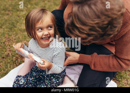 Smiling girl sitting avec son père à l'extérieur tenant un bâton de sucre candy. Père et fille de passer du temps ensemble manger du sucre candy. Banque D'Images