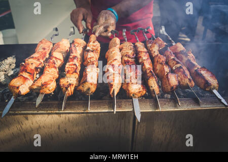 Sur le barbecue, beaucoup de viande est rôti sur les brochettes, le chef remet son shish kebabs. La main d'un homme tourne, frites viandes savoureuses brochettes de porc sur dans Banque D'Images