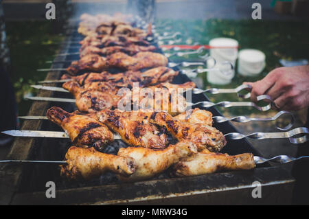 Cuisses de poulet marinées au plat sur le feu chaud Barbecue. Le charbon de flammes sur l'arrière-plan. chef tourne shish kebab sur une brochette. La cuisson du poulet sur t Banque D'Images