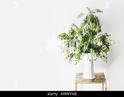 Bouquet de fleurs avec des branches d'acacia en fleurs dans un vase au mur blanc. Design intérieur simple et des idées . Still Life Banque D'Images