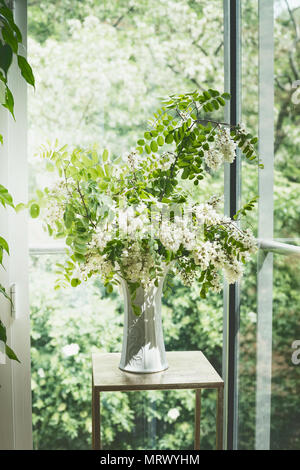 De belles fleurs bouquet de fleurs avec des branches d'acacia dans vase blanc dans la salle de séjour à fenêtre. Architecture d'intérieur et d'idées . Still Life Banque D'Images