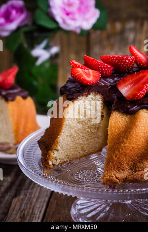 Gâteau bundt fait maison avec ganache chocolat glacé et de fraises fraîches sur le dessus de table en bois rustique Banque D'Images