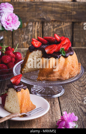 Gâteau bundt fait maison avec ganache chocolat glacé et de fraises fraîches sur le dessus de table en bois rustique Banque D'Images