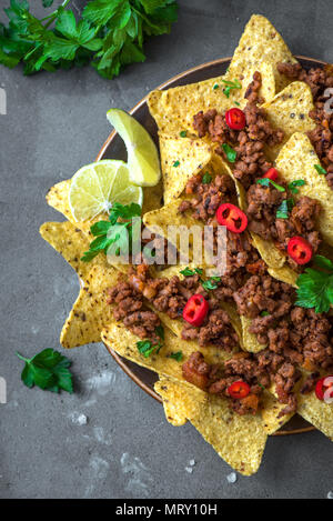 Nacho chips tortilla Maïs mexicain avec le fromage, la viande, le guacamole et red hot salsa épicée. Nachos avec du boeuf haché sur fond sombre, copie espace rustique. Banque D'Images