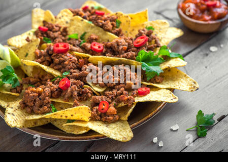 Nacho chips tortilla Maïs mexicain avec le fromage, la viande, le guacamole et red hot salsa épicée. Nachos avec du boeuf haché sur fond sombre, copie espace rustique. Banque D'Images