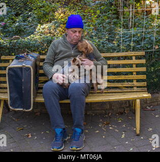 Homeless man avec son petit chien et ses affaires s'asseoir sur un banc dans un parc jaune image avec l'espace de copie au format paysage Banque D'Images