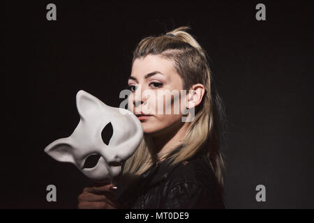 Jeune femme tenant un masque chats sur fond sombre Banque D'Images
