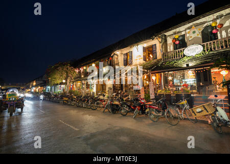 Scooters en stationnement, un tuktuk et des gens assis, in lit époque coloniale française des constructions qui sont transformés en restaurants et cafés à Luang Prabang, Laos. Banque D'Images