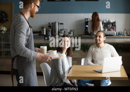 Waiter carrying café pour smiling couple en attente à cafe table Banque D'Images