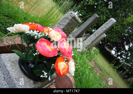 Un bouquet de fleurs artificielles colorées s'asseoir sur le dessus d'une fosse dans le parc du cimetière de drumbrae à Édimbourg Banque D'Images