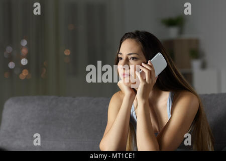 Bored femme en attente durant un appel téléphonique assis sur un canapé dans la salle de séjour à la maison Banque D'Images