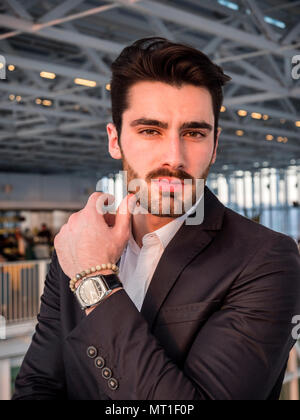 Handsome serious businessman standing dans un immeuble moderne à côté de la fenêtre, looking at camera Banque D'Images